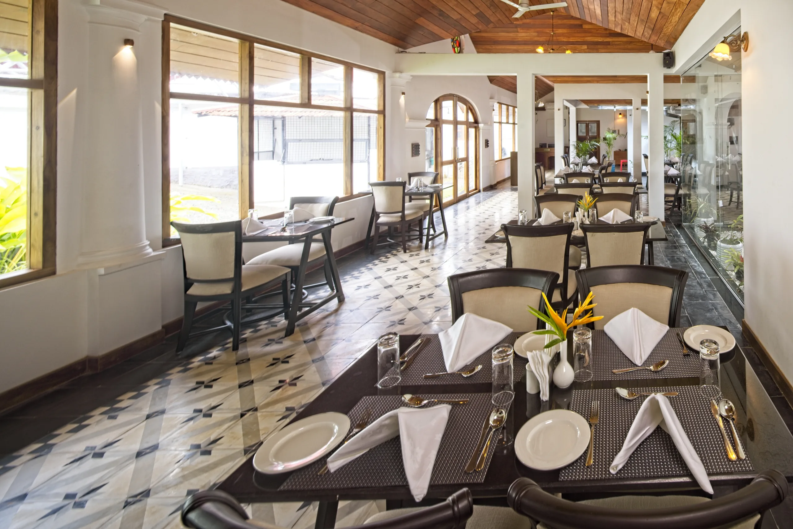 The Kohinoor dining room, with tables laid in white linen and cutlery beside tall windows looking onto the garden.