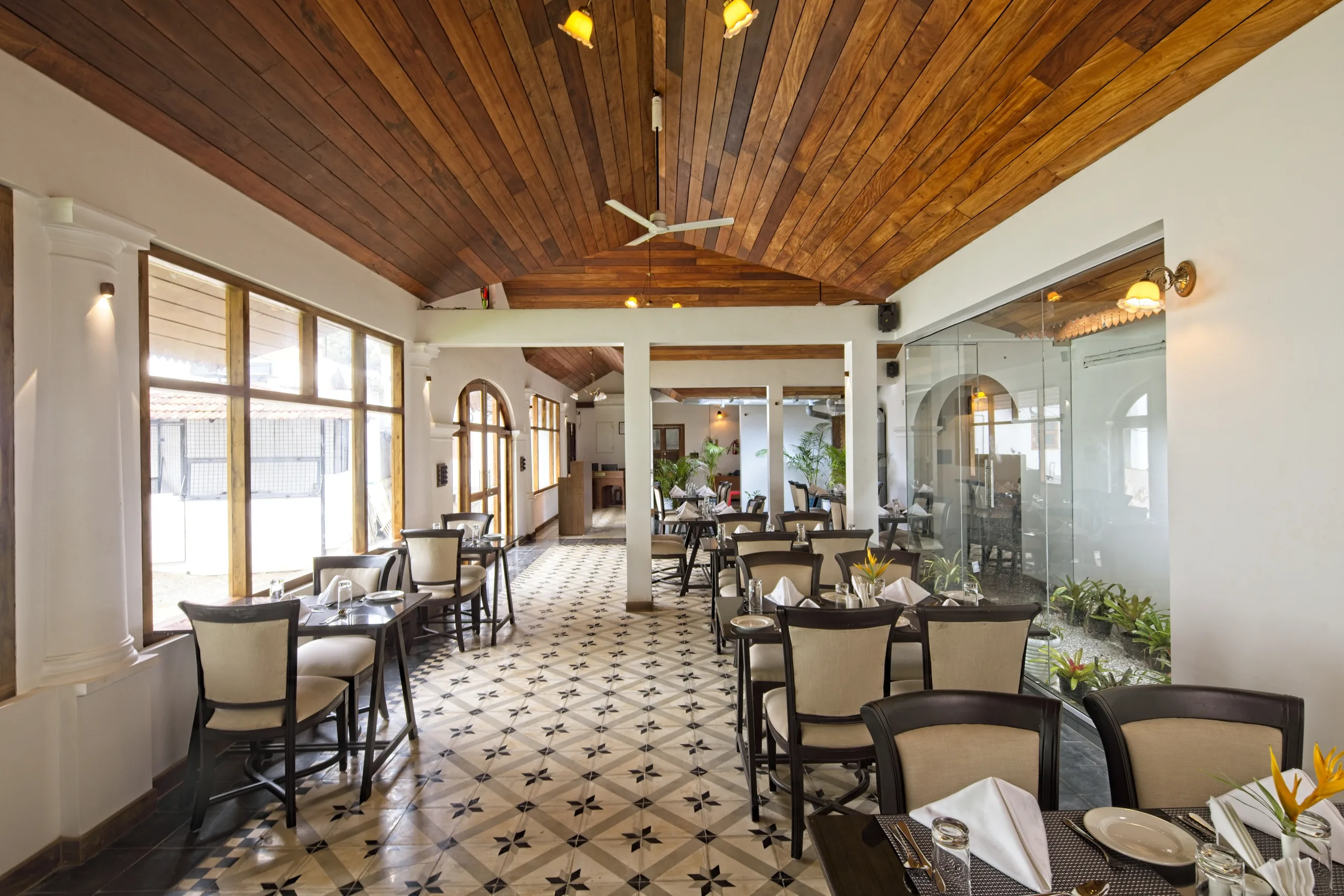 The Kohinoor dining room under a pitched teak ceiling, with dark wood tables, cream upholstered chairs and a patterned tile floor.