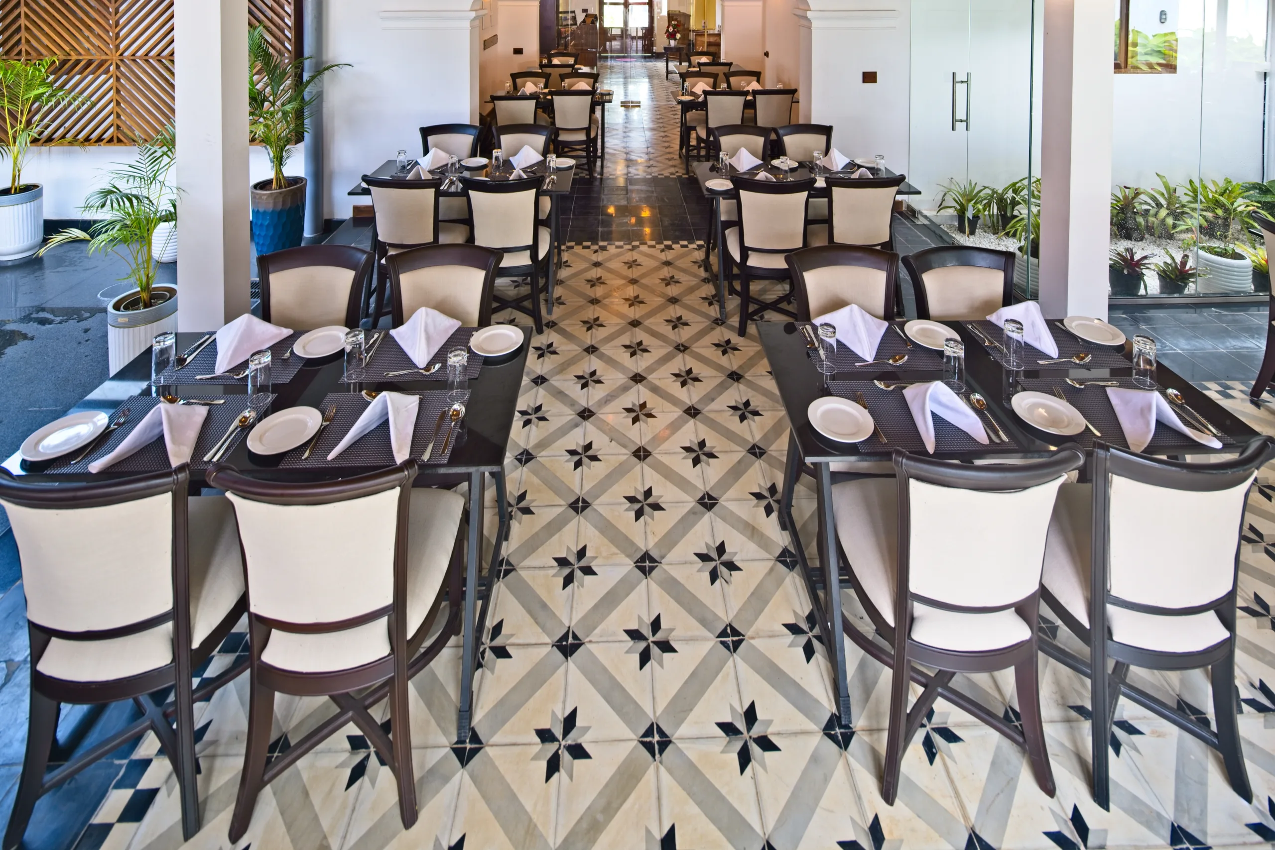 Tables laid for service in the Kohinoor dining room, on a star-patterned tile floor between potted palms.