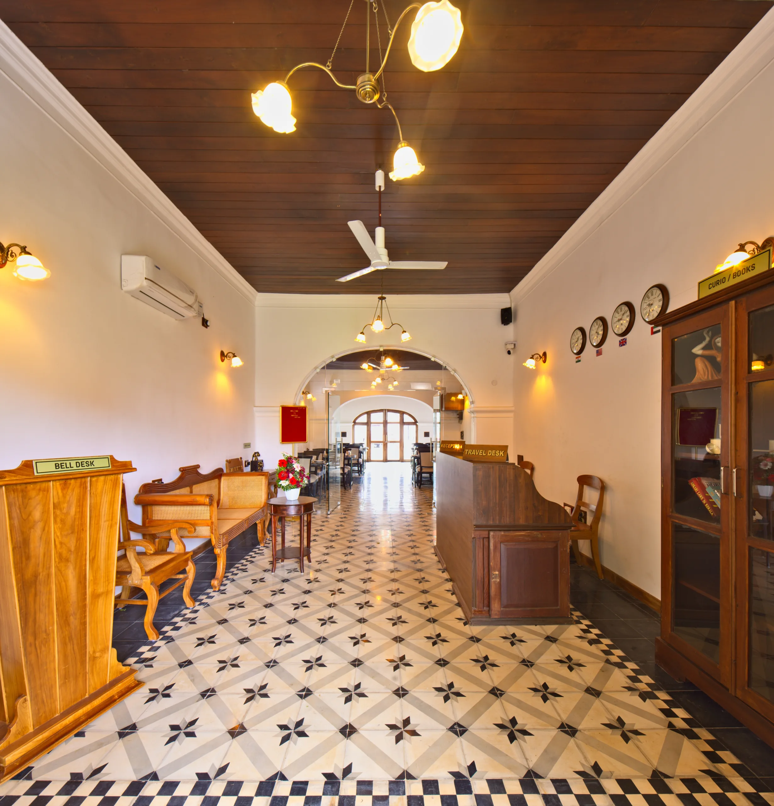 The reception hall, with a bell desk and travel desk in polished wood, a row of world clocks on the wall, a glazed curio cabinet and a star-patterned tile floor.